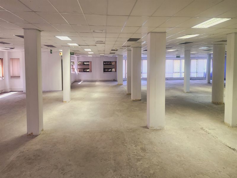 A large, open-plan office space featuring a suspended ceiling, structural columns, and expansive windows with vertical blinds, currently in a shell condition.