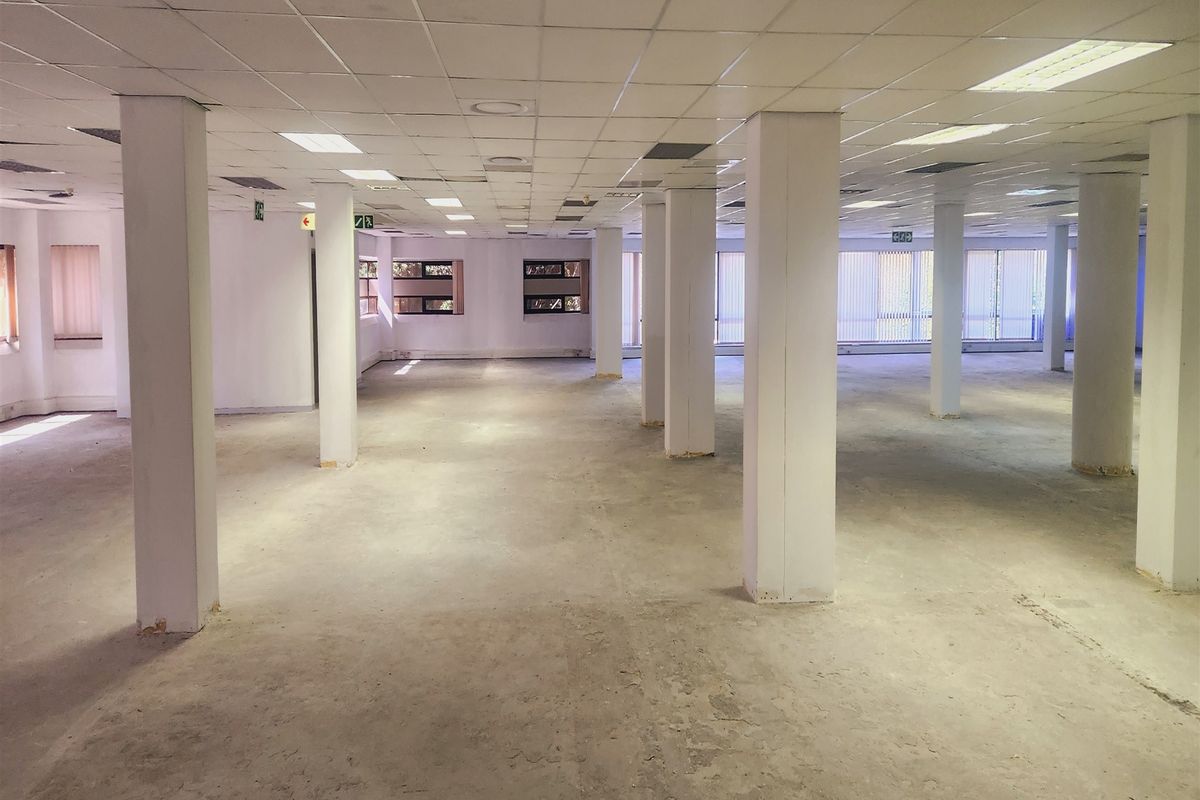 A large, open-plan office space featuring a suspended ceiling, structural columns, and expansive windows with vertical blinds, currently in a shell condition.