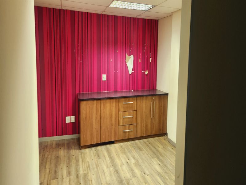 A small office space featuring built-in wooden cabinetry, wood-look laminate flooring, and a distinctive red striped feature wall with visible surface damage.