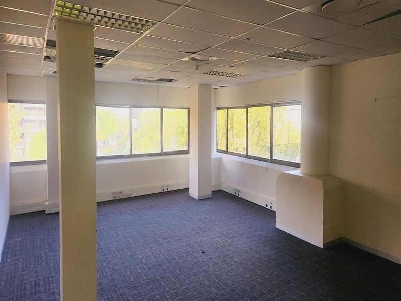 An empty office space featuring carpet tiles, perimeter trunking, and large windows with natural light, requiring minor ceiling and wall maintenance.