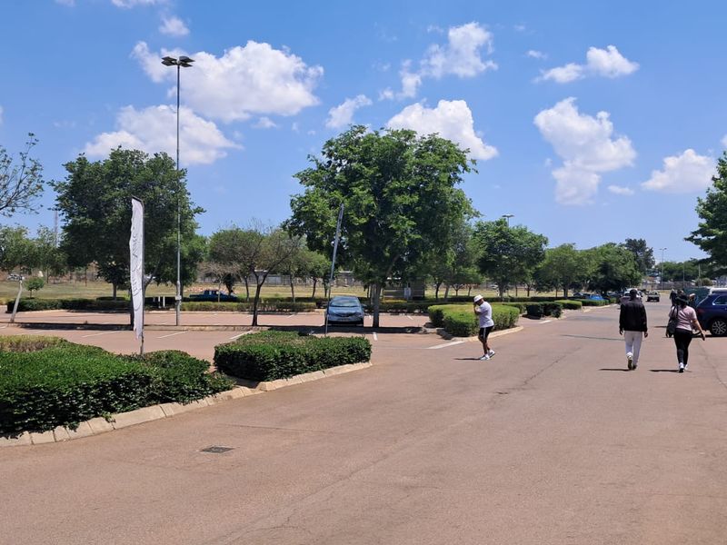 An outdoor parking area for the retail property featuring paved surfaces, landscaped garden beds, and tall lighting poles.