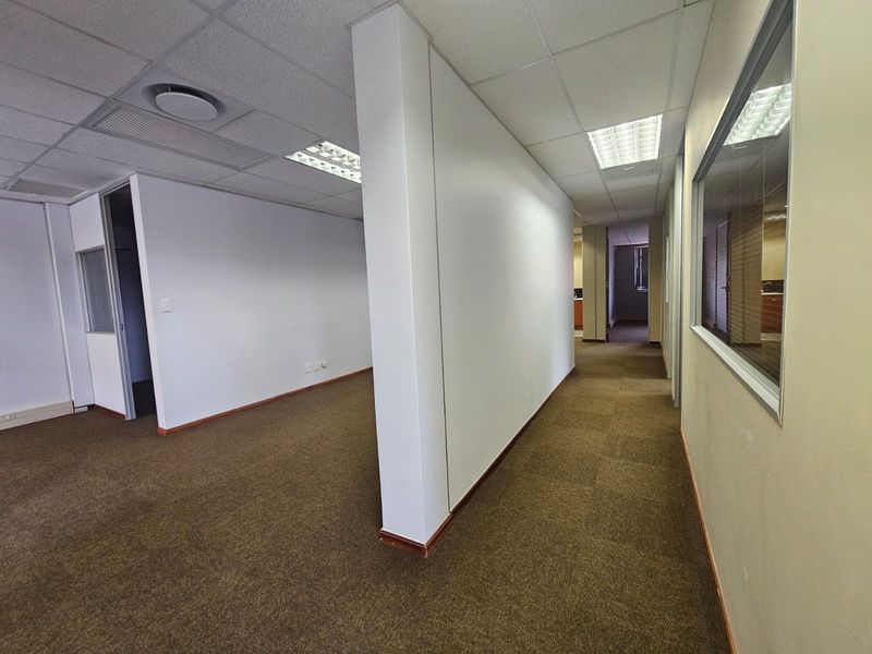 An empty office space featuring neutral partition walls, suspended ceilings with recessed lighting, and carpeted flooring throughout.