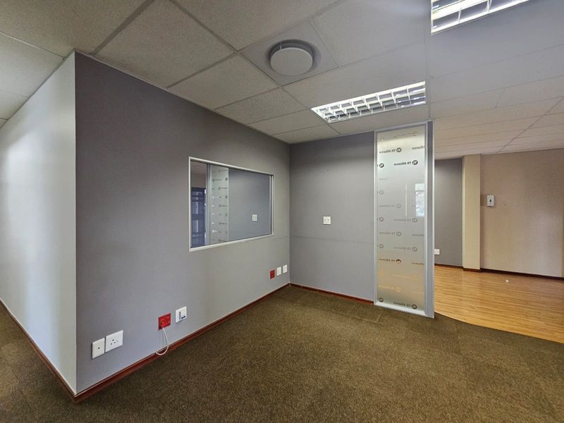 An empty office space featuring a mix of carpet and laminate flooring, a frosted glass partition, and an internal window for natural light.
