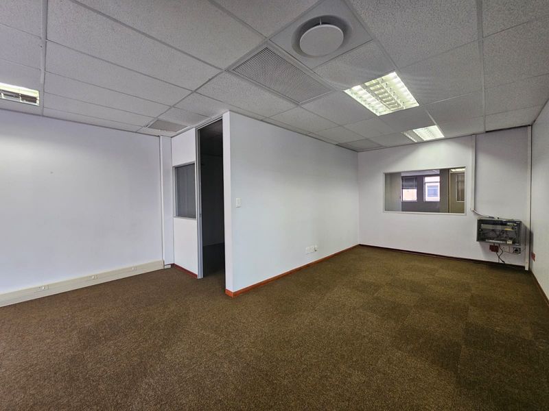 An empty office space featuring carpeted flooring, a suspended ceiling with recessed lighting, and an internal partition wall with a window.