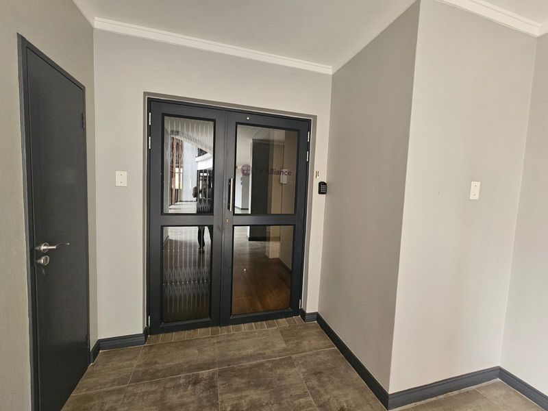 A clean and professional office entrance featuring double glass doors with integrated keypad access control and neutral wall finishes.