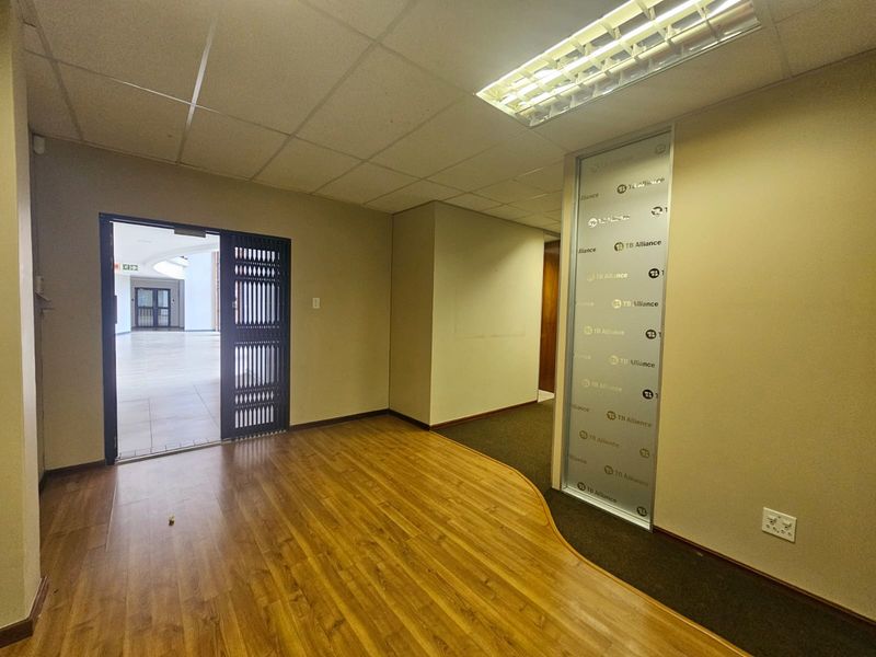 An empty office space featuring a mix of laminate and carpet flooring, a suspended ceiling with integrated lighting, and a frosted glass partition.