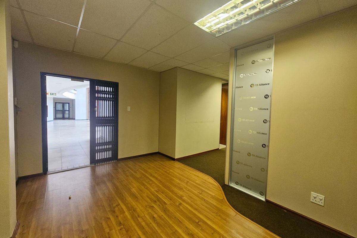 An empty office space featuring a mix of laminate and carpet flooring, a suspended ceiling with integrated lighting, and a frosted glass partition.