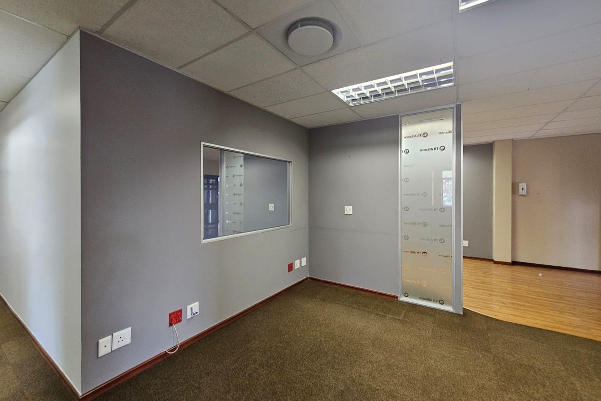 An empty office space featuring a mix of carpet and laminate flooring, a frosted glass partition, and an internal window for natural light.