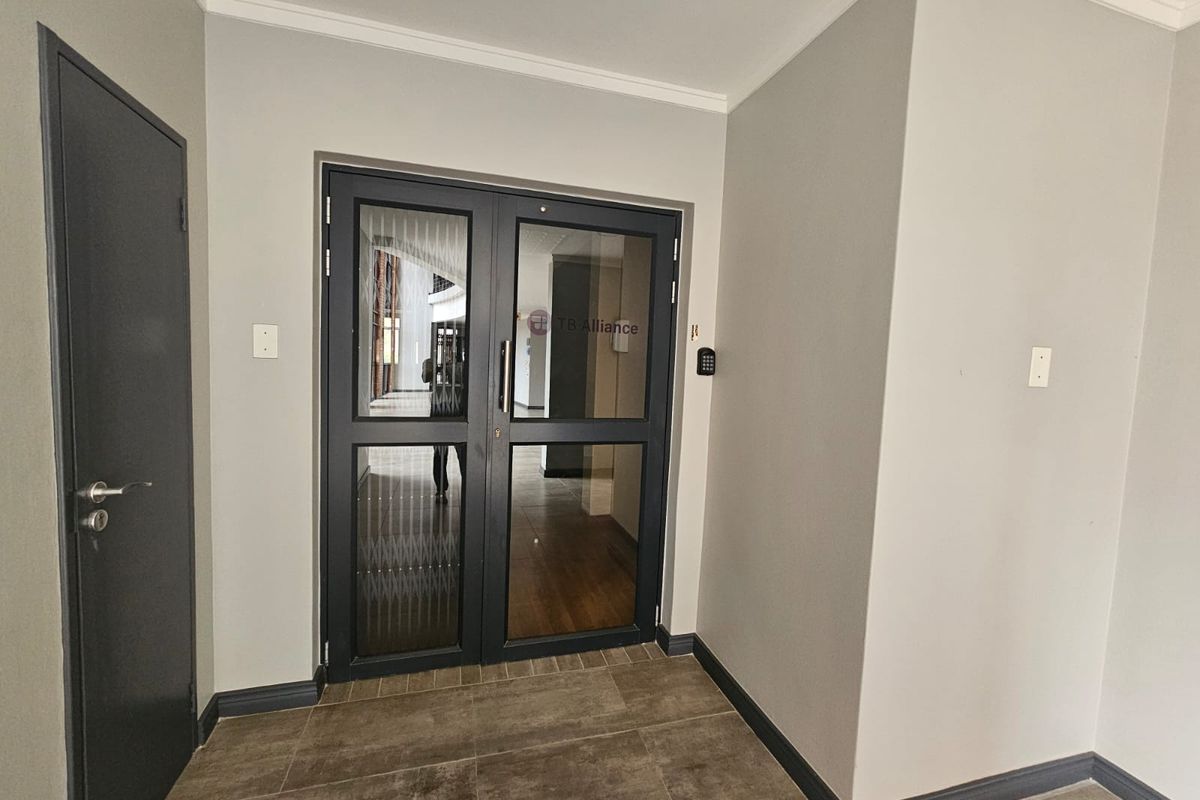 A clean and professional office entrance featuring double glass doors with integrated keypad access control and neutral wall finishes.