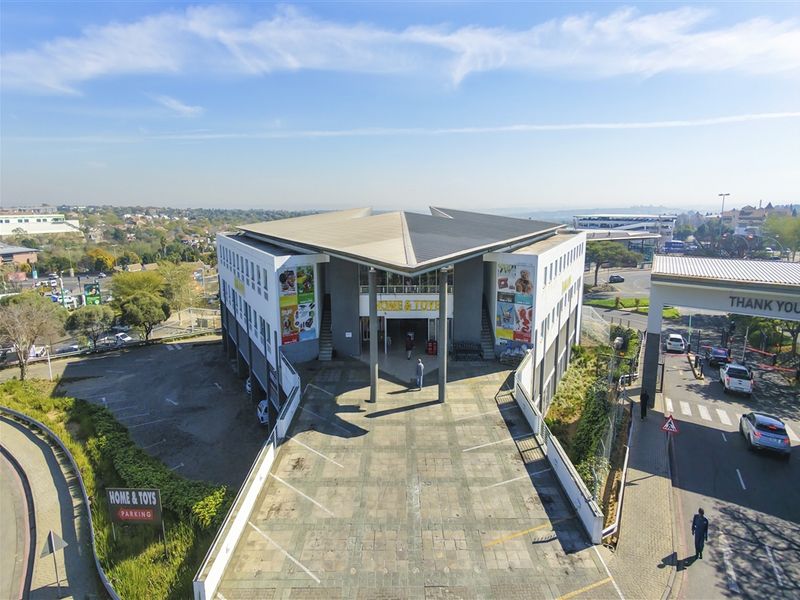 Aerial view of a commercial office building featuring a paved parking area, secure gated entrance, and modern architectural design.