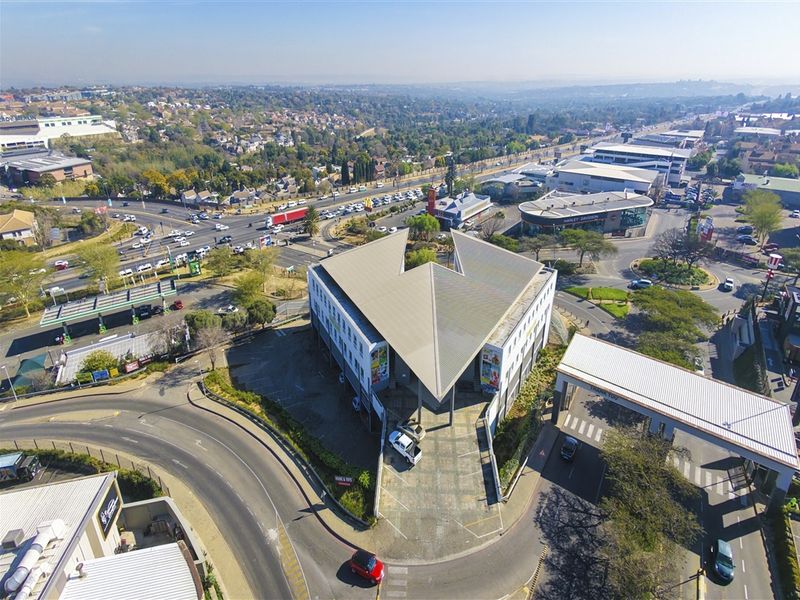 Aerial view of a commercial office building featuring a distinctive V-shaped roof design, paved parking area, and surrounding urban infrastructure.