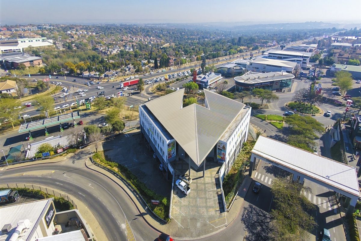 Aerial view of a commercial office building featuring a distinctive V-shaped roof design, paved parking area, and surrounding urban infrastructure.