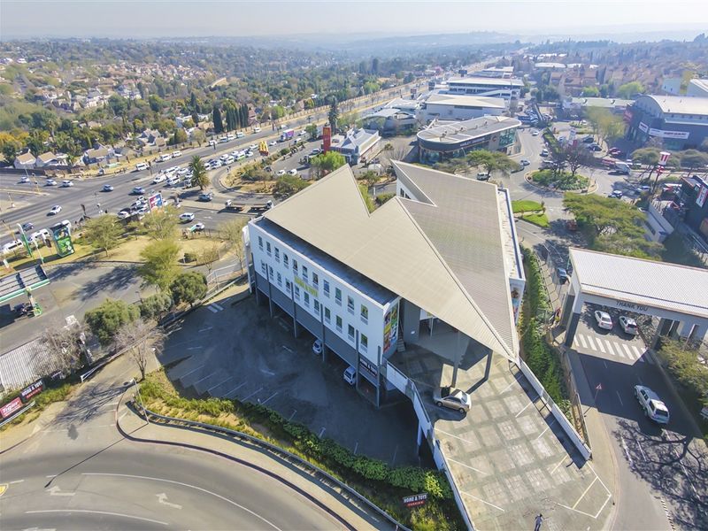 Aerial view of a commercial office building featuring a distinctive angular roof design, ample parking space, and convenient access to major road networks.