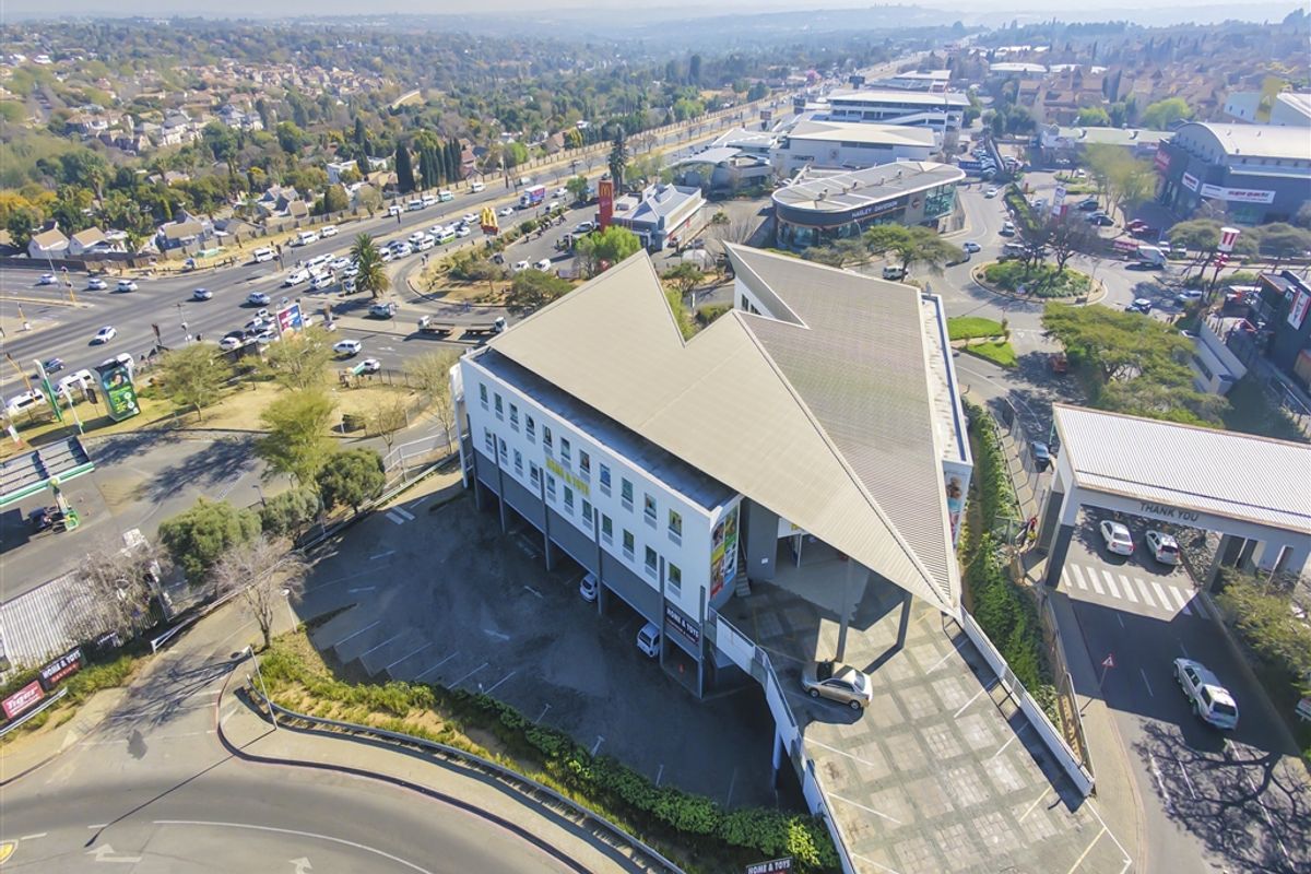 Aerial view of a commercial office building featuring a distinctive angular roof design, ample parking space, and convenient access to major road networks.