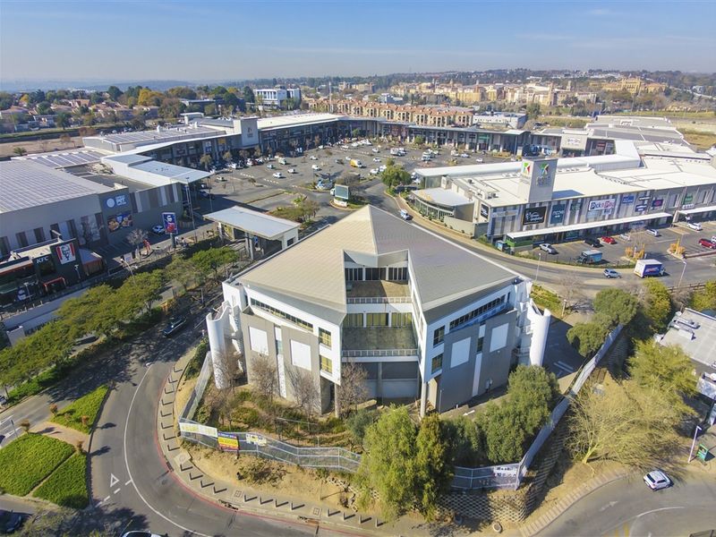 Aerial view of a commercial office building situated adjacent to a large retail shopping center and parking area.