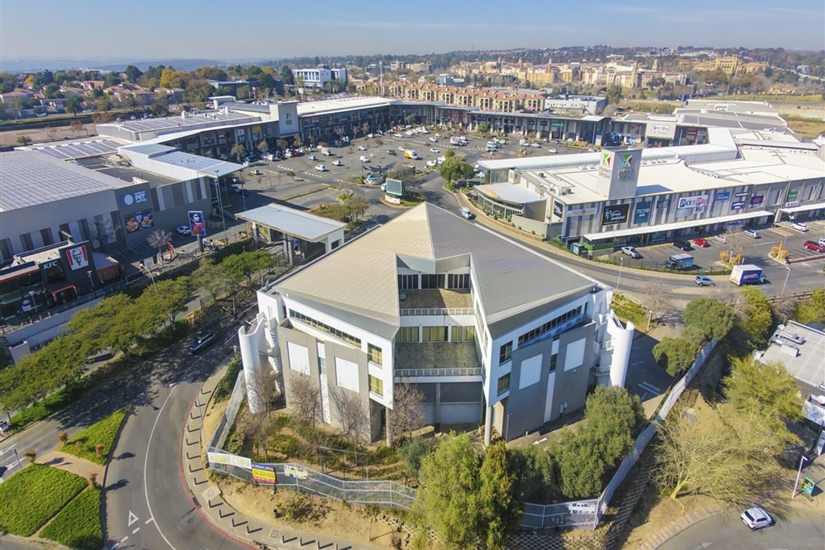 Aerial view of a commercial office building situated adjacent to a large retail shopping center and parking area.