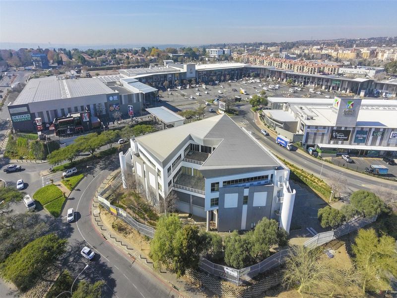 Aerial view of a commercial office building situated within a retail and business precinct, featuring ample parking and modern architectural design.