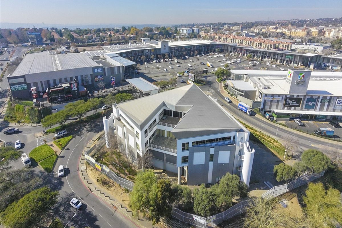 Aerial view of a commercial office building situated within a retail and business precinct, featuring ample parking and modern architectural design.