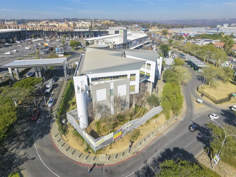 Aerial view of a modern multi-story office building situated on a corner lot with perimeter fencing and surrounding road infrastructure.