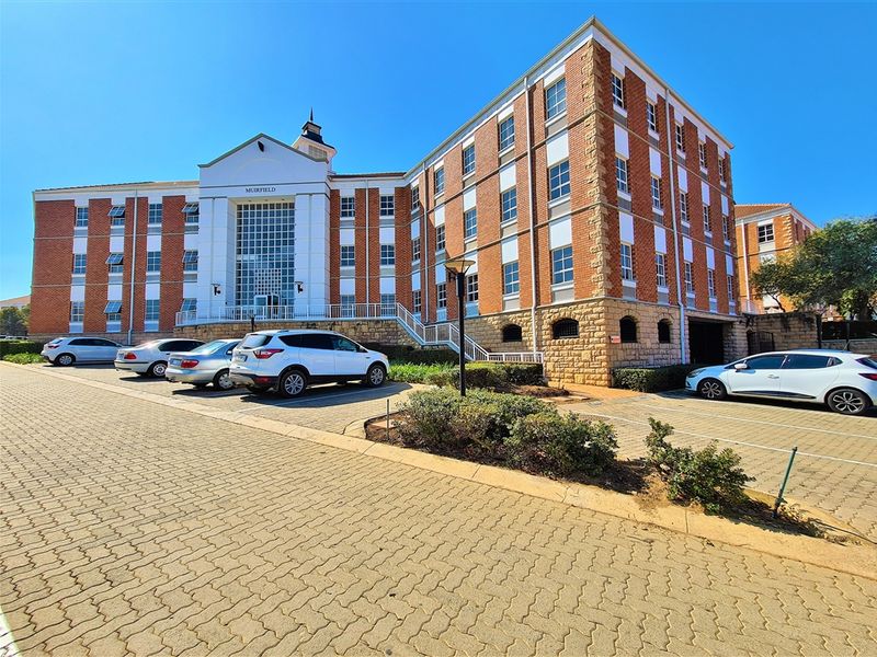 Front elevation of the Muirfield office building featuring a multi-story brick and stone facade with an integrated paved parking area.