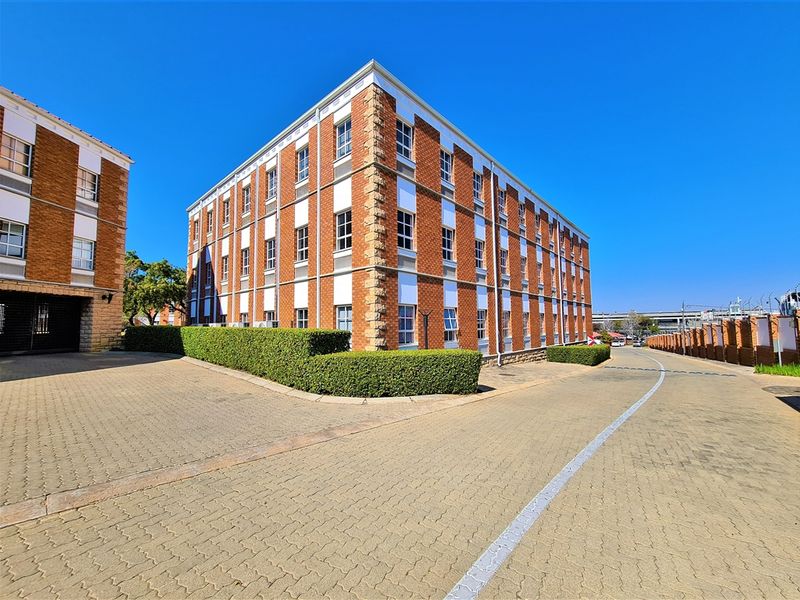 A multi-story office building featuring a classic brick facade, well-maintained hedges, and a paved driveway entrance.