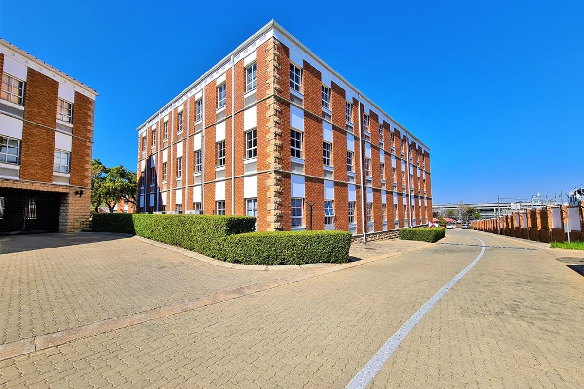 A multi-story office building featuring a classic brick facade, well-maintained hedges, and a paved driveway entrance.