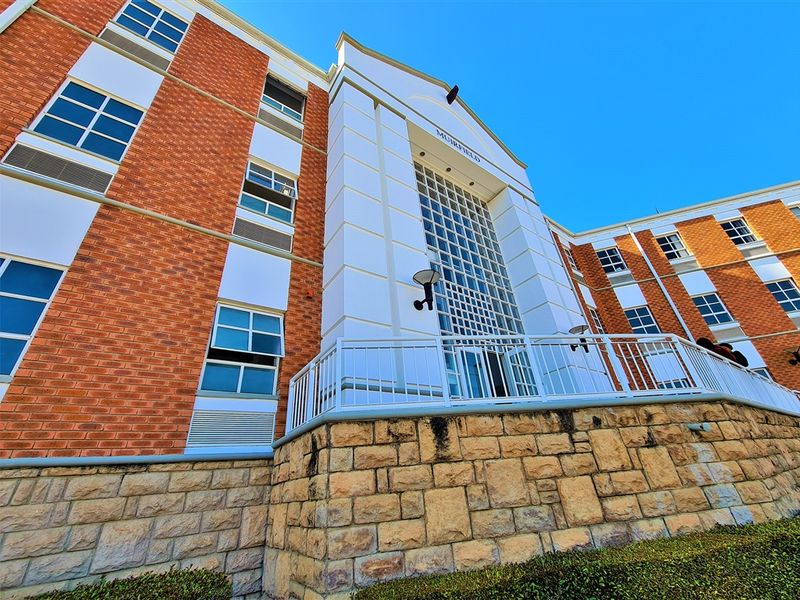 Low angle view of the Muirfield office building facade featuring red brickwork, a stone masonry base, and a prominent glass block entrance section.