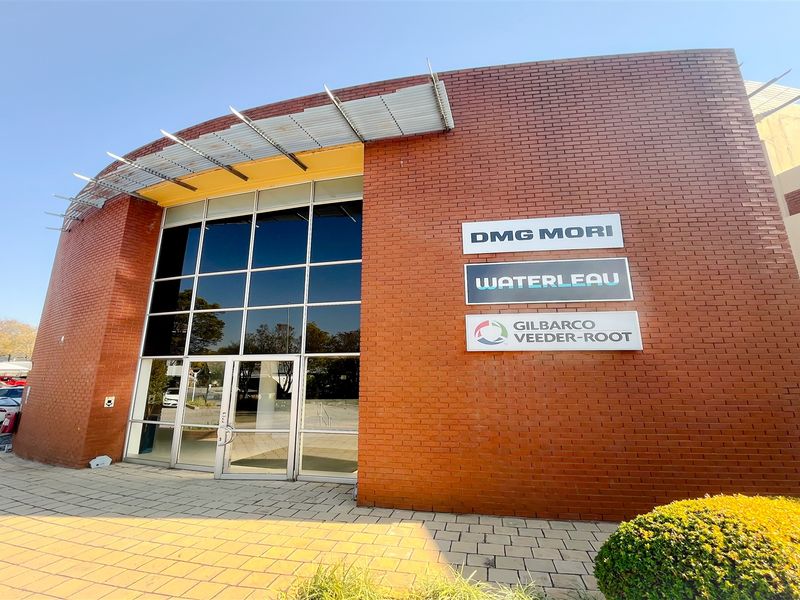 Front exterior view of a modern office building featuring a prominent brick facade, large glass entrance, and professional commercial signage.