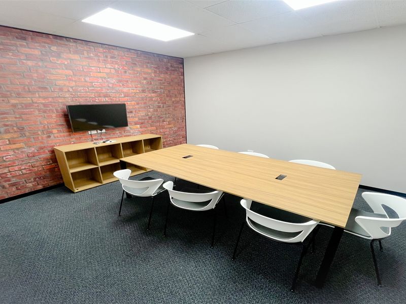 A professional office meeting room featuring a brick accent wall, recessed ceiling lighting, and carpeted flooring.