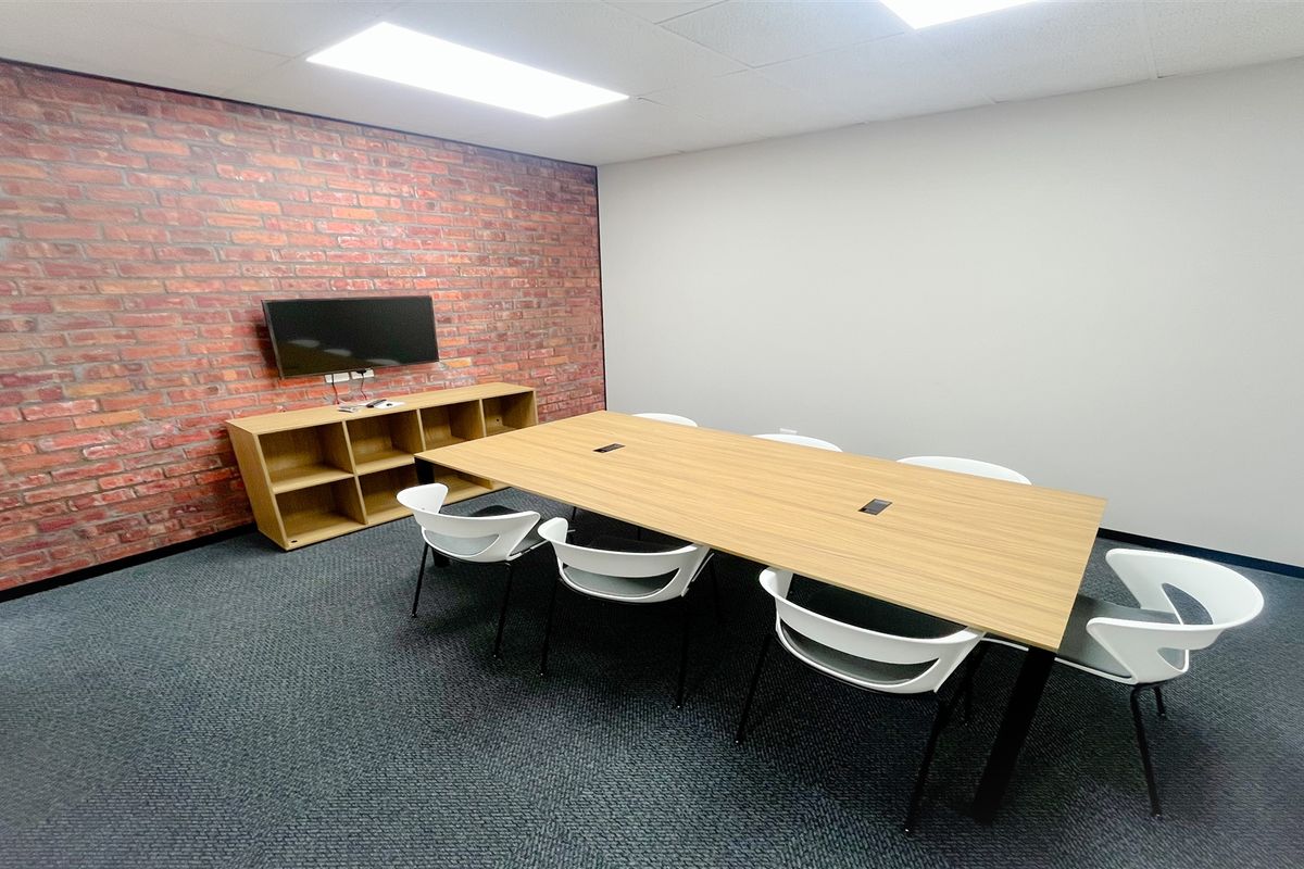 A professional office meeting room featuring a brick accent wall, recessed ceiling lighting, and carpeted flooring.