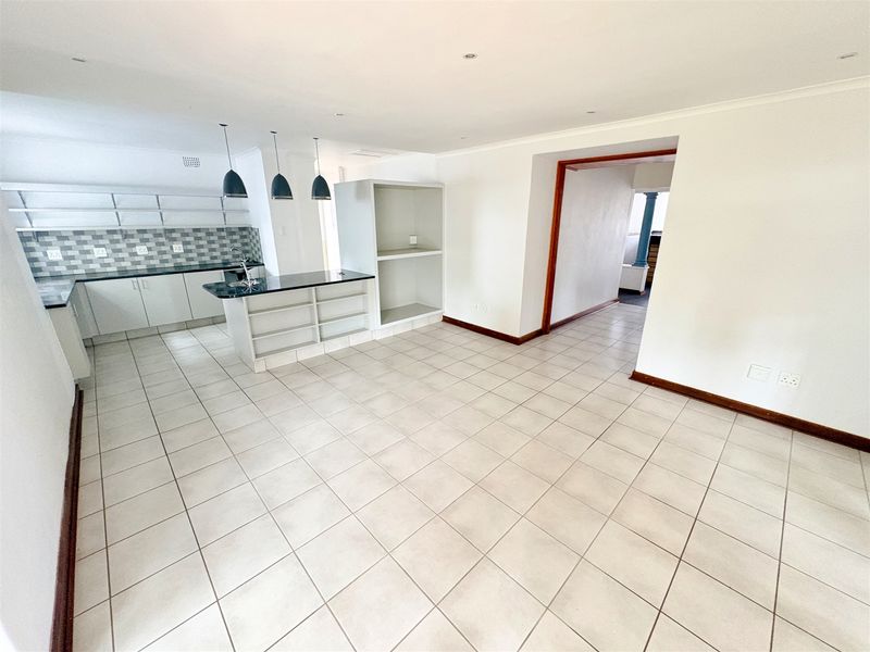 Spacious open-plan office area featuring tiled flooring, a functional kitchen island with sink, and built-in cabinetry, offering a clean and versatile workspace.