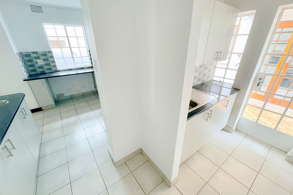 A clean, functional kitchen area featuring white cabinetry, dark granite countertops, tiled flooring, and direct access to an outdoor space.