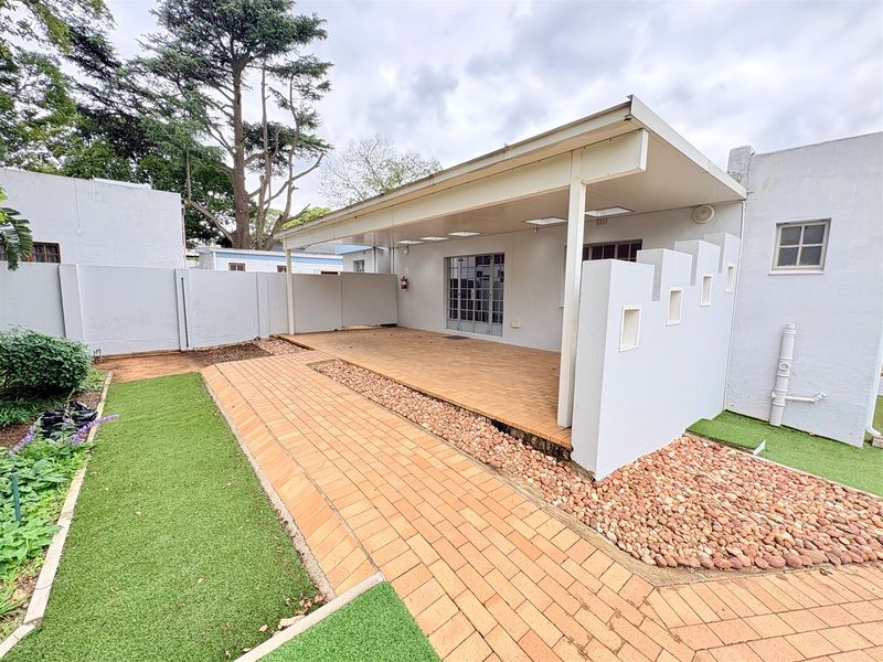 A well-maintained rear exterior area featuring a covered patio, brick-paved pathways, and low-maintenance artificial lawn sections.