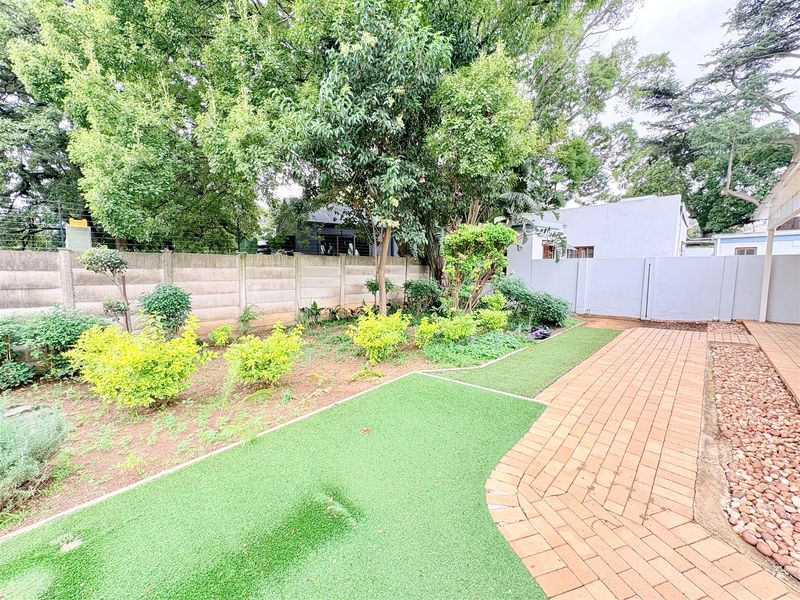 A well-maintained garden area featuring artificial turf, a paved walkway, pebble borders, and a secure precast concrete perimeter wall.