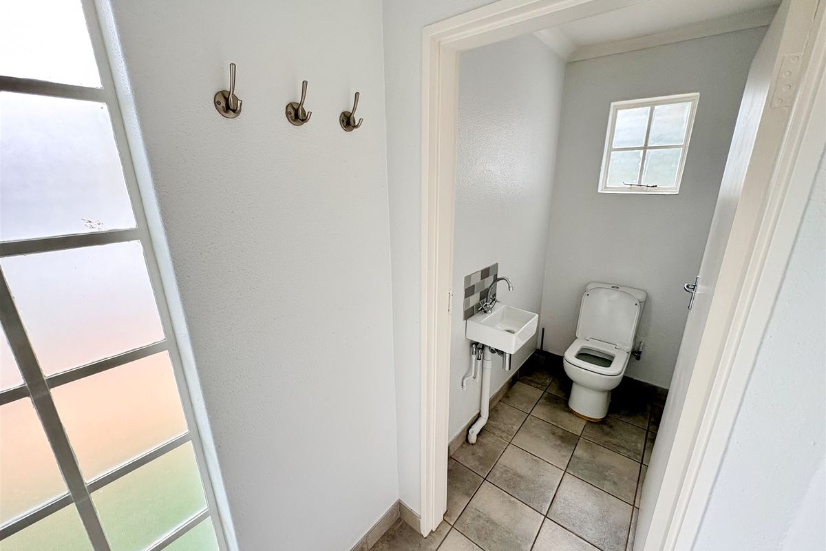 A clean and functional guest bathroom featuring a wall-mounted basin, toilet, tiled flooring, and a small frosted window for natural light.