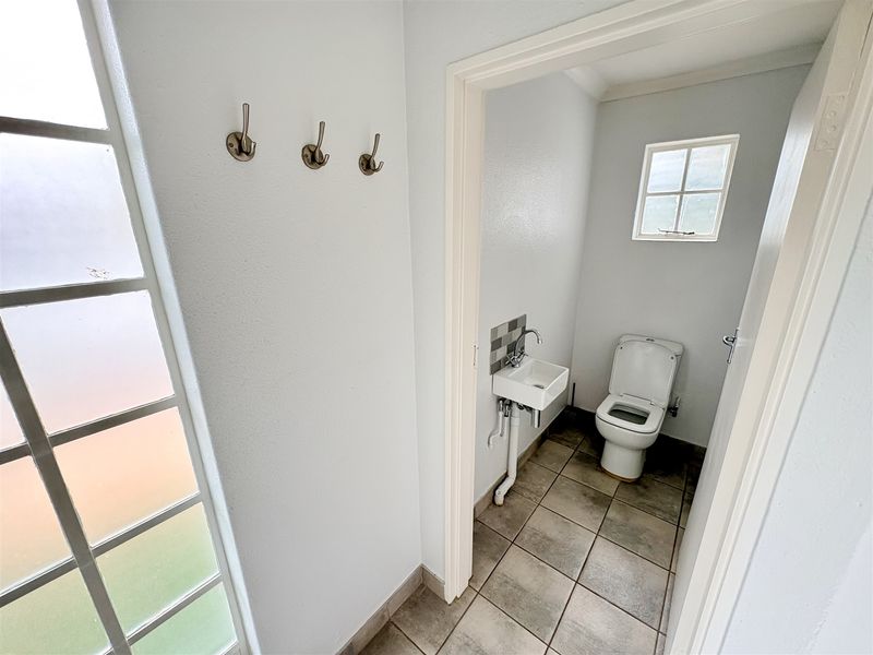A clean and functional guest bathroom featuring a wall-mounted basin, toilet, tiled flooring, and a small frosted window for natural light.