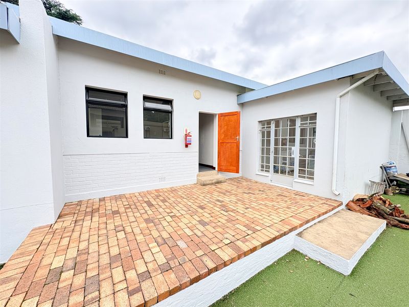 Rear exterior view of the office building featuring a brick-paved patio, white painted masonry walls, and access via a timber door.