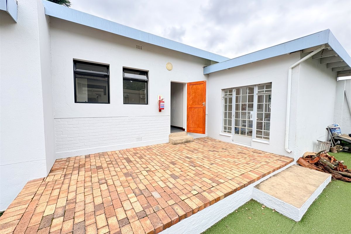 Rear exterior view of the office building featuring a brick-paved patio, white painted masonry walls, and access via a timber door.