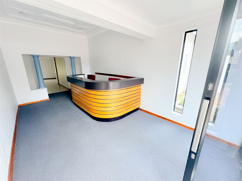 A bright office entrance area featuring a built-in reception desk, decorative columns, and carpeted flooring.