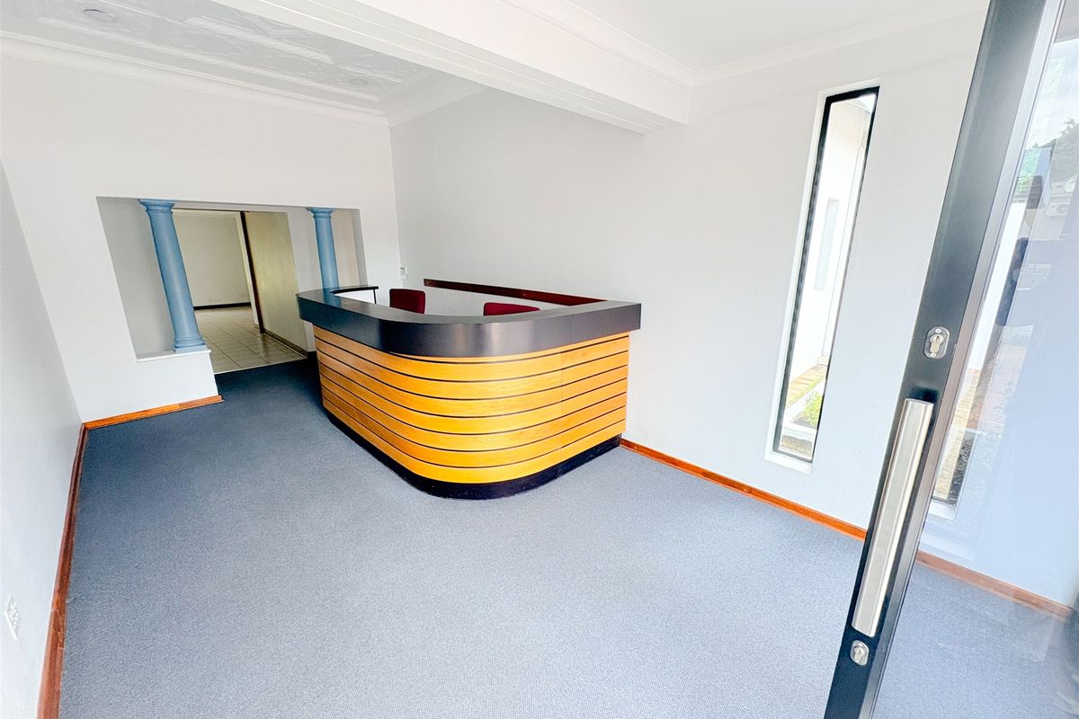 A bright office entrance area featuring a built-in reception desk, decorative columns, and carpeted flooring.