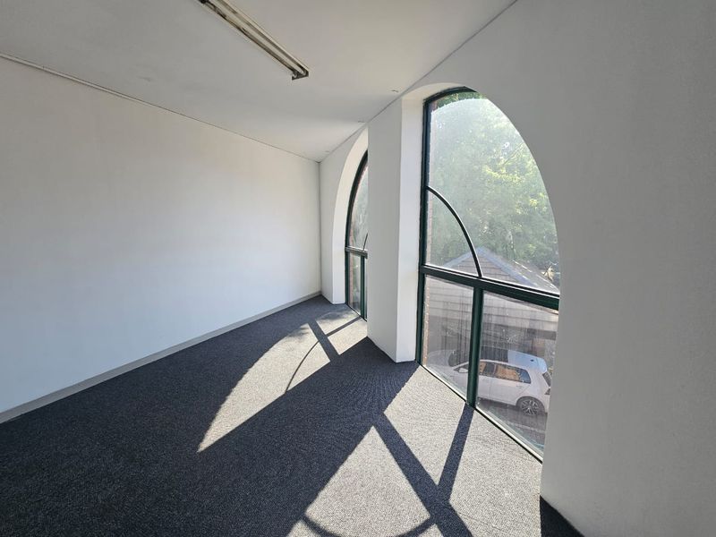 A bright, empty office space featuring distinctive arched windows and carpeted flooring, suitable for a professional workspace.