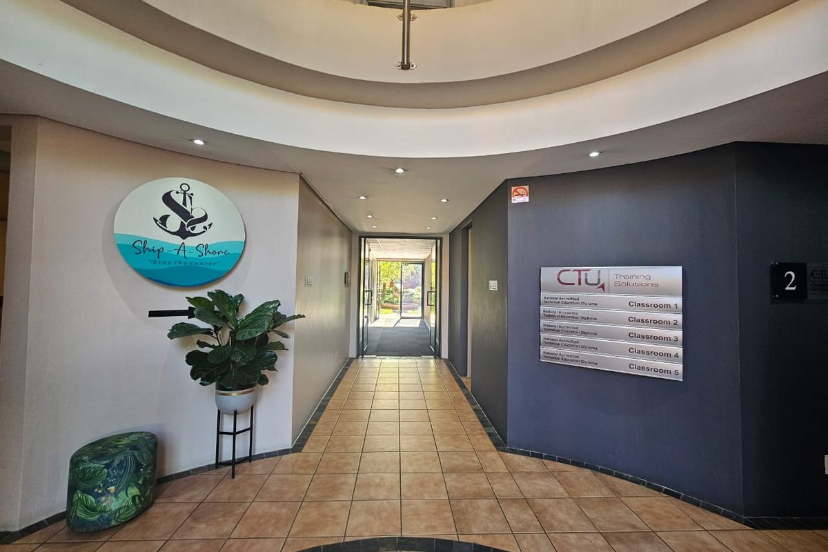 A well-lit commercial hallway featuring tiled flooring, directional signage for classrooms, and a distinctive circular architectural ceiling design.