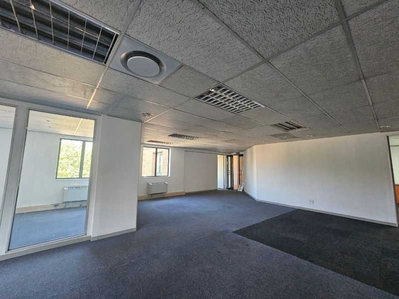 An open-plan office space featuring a suspended ceiling, recessed lighting, air conditioning units, and glass partitioning, offering a versatile layout for business operations.