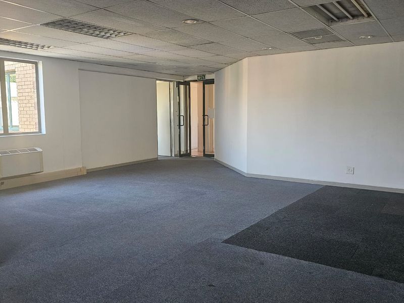 An empty, open-plan office space featuring a suspended ceiling, recessed lighting, and carpeted flooring with an integrated air conditioning unit.