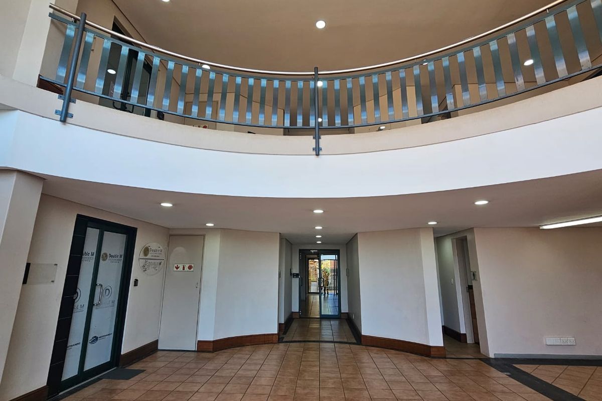 Spacious commercial entrance foyer featuring a mezzanine level with metal balustrade, tiled flooring, and recessed lighting, providing a professional and open reception area.
