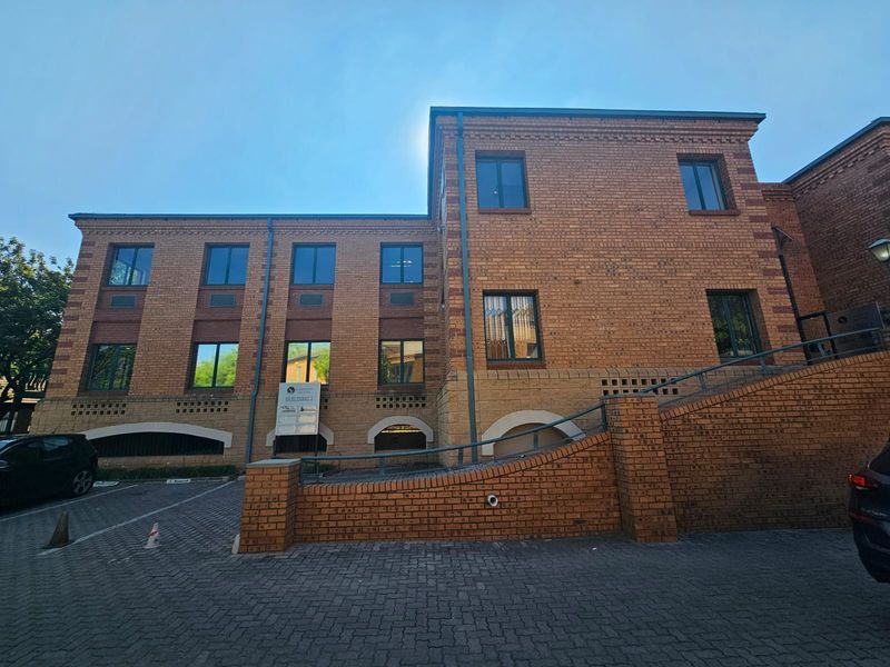 A multi-story commercial brick building featuring a paved driveway, external staircase with metal handrails, and multiple windows.