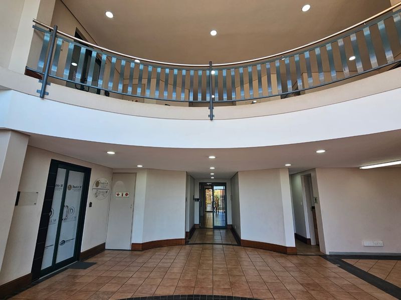 Spacious commercial entrance foyer featuring a mezzanine level with metal balustrade, tiled flooring, and recessed lighting, providing a professional and open reception area.