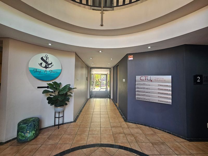 A well-lit commercial hallway featuring tiled flooring, directional signage for classrooms, and a distinctive circular architectural ceiling design.