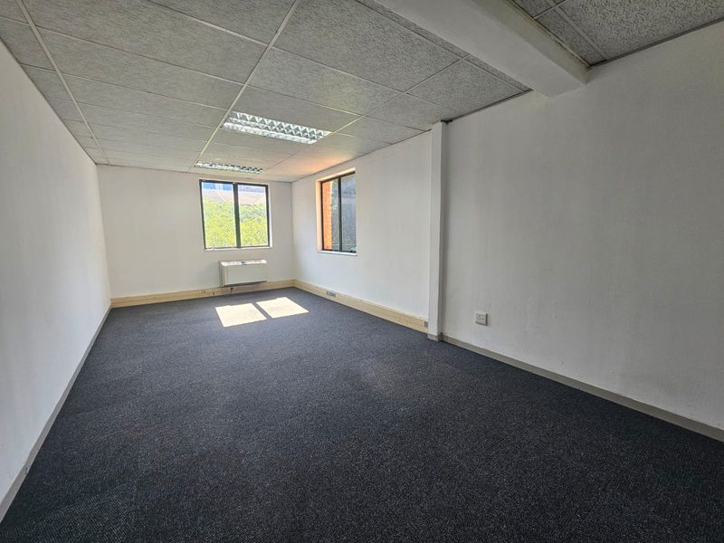 A vacant office space featuring a suspended ceiling, recessed lighting, carpeted flooring, and a wall-mounted air conditioning unit.