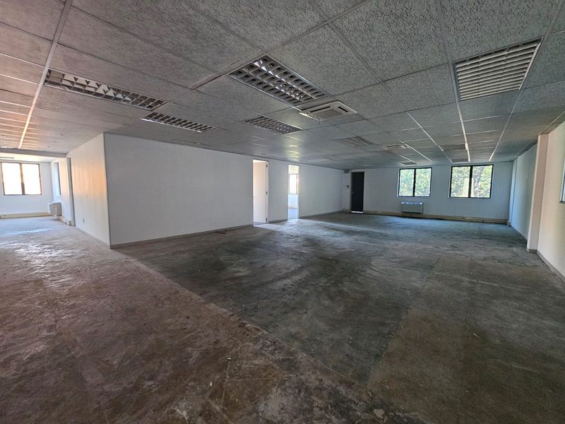 A large, vacant open-plan office space featuring a suspended ceiling with recessed lighting, HVAC units, and large windows, ready for custom flooring and fit-out.
